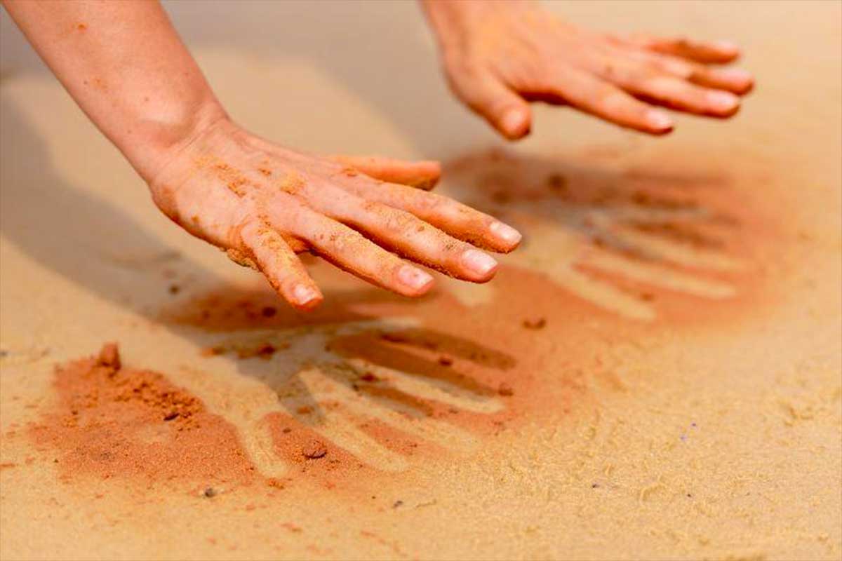 Hands pressing down on wet beach sand